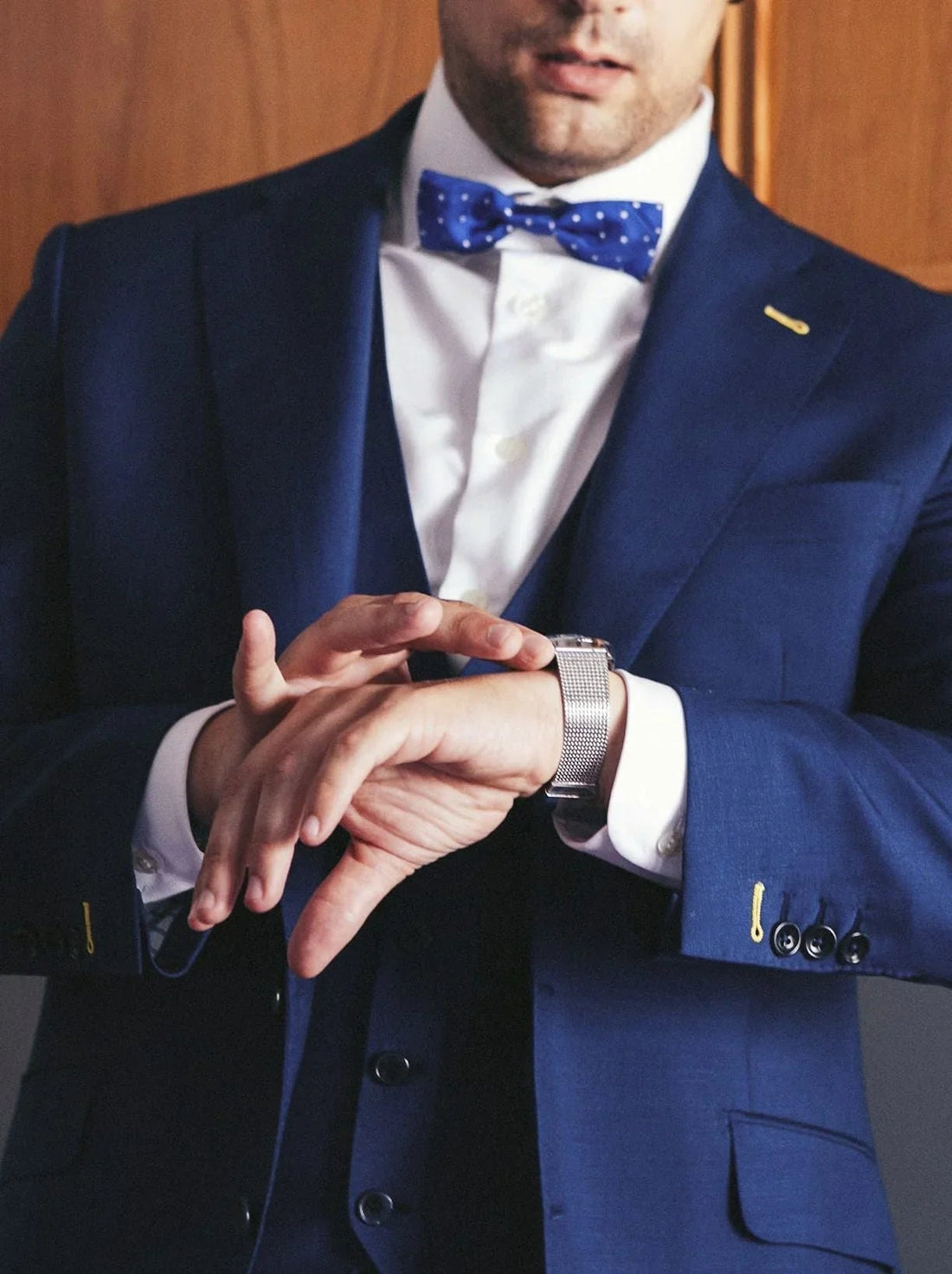 Hombre con traje azul y pajarita azul con puntos blancos ajustándose reloj de pulsera plateado