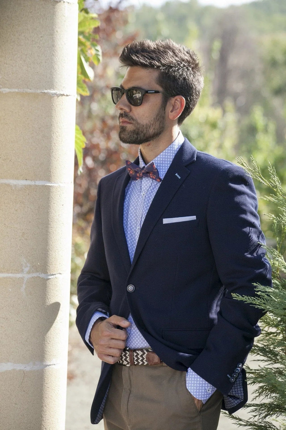 Hombre con pajarita estampada roja, chaqueta azul y gafas de sol, estilo elegante y original