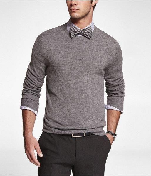 Hombre con pajarita de cuadros gris y blanco, jersey gris y camisa con mangas remangadas, look elegante y casual