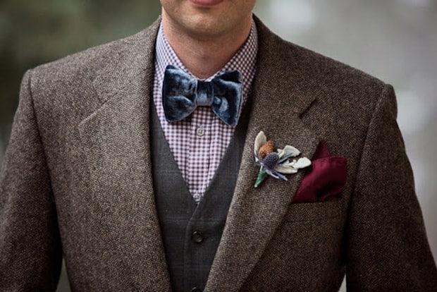 Hombre con pajarita azul de terciopelo y traje marrón con chaleco y flores en la solapa, estilo elegante y original