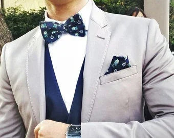 Hombre vestido con pajarita azul estampada, chaqueta beige y chaleco azul, elegante y moderno